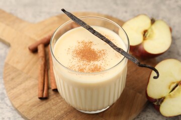 Delicious protein shake in glass, apples, cinnamon and vanilla pods on grey table, closeup