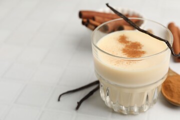 Delicious protein shake in glass, cinnamon and vanilla pods on white tiled table, closeup. Space for text