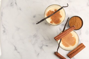Delicious protein shake in glasses, cinnamon and vanilla pods on white marble table, flat lay. Space for text