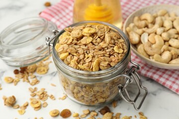 Tasty granola in glass jar on white marble table, closeup