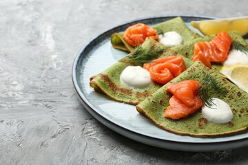 Tasty spinach crepes with salmon, sour cream, dill and lemon on grey table, closeup. Space for text