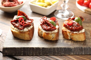 Delicious bruschettas with cream cheese, sun-dried tomatoes, chili pepper and green olives on wooden table, closeup