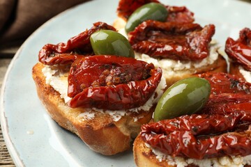 Delicious bruschettas with cream cheese, sun-dried tomatoes and green olives on table, closeup