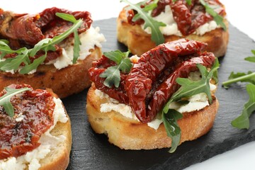 Delicious bruschettas with cream cheese, sun-dried tomatoes and arugula on table, closeup