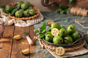 A rustic still life with ripe pineapple guavas, some cut open to reveal the fleshy pulp, on a small...