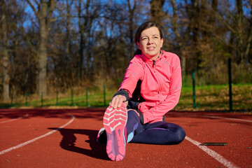 Woman sitting on running track stretching leg and holding foot