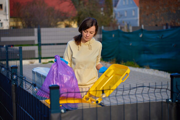 Woman wearing gloves placing garbage bag into outdoor recycling container