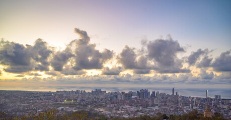 Panoramic view of a city along the coastline during a vibrant sunset, highlighting urban architecture, water reflections, and warm evening light. Perfect for travel, cityscape, or coastal projects.