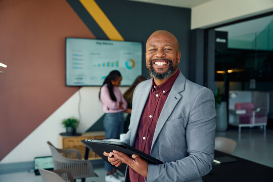 Happy black mature businessman with digital tablet in boardroom at workplace
