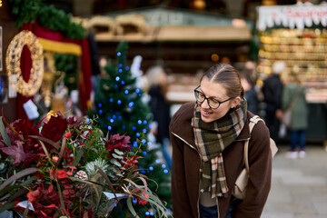 Cheerful young woman looking for New Year decorations in traditional street market