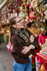 Cheerful young woman looking for New Year decorations in traditional street market