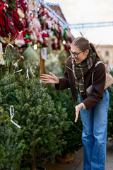 Cheerful young woman looking for New Year decorations in traditional street market