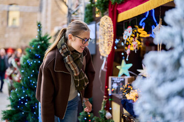 Cheerful young woman looking for New Year decorations in traditional street market