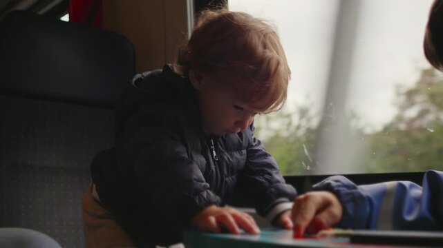 Toddler leaning over small train table exploring objects with focused curiosity while carriage moves creating lively moment of early engagement and playful attention during travel