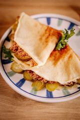 Savory crepes with minced meat, pickles and lettuce served on ceramic plate. Close-up composition with soft focus and warm natural light.