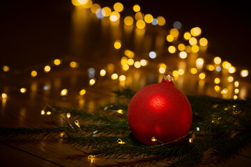 A red Christmas bauble resting on pine branches with warm golden bokeh lights in the background.
