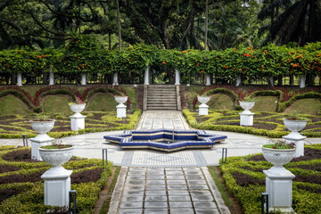 Empty alley in Perdana public botanical park in Kuala Lumpur, Malaysia. Formal garden with round fountain and flower pots, no people. 
