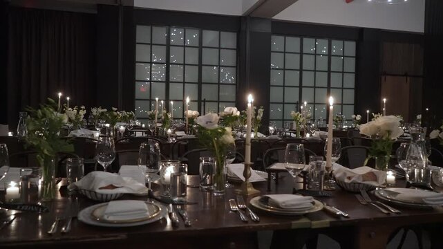 Formal Long Table Dinner In Loft, Event Planner Finalizing Seating, MaTre D Adjusting Candles, Caterer Inspecting Glassware Candlelit