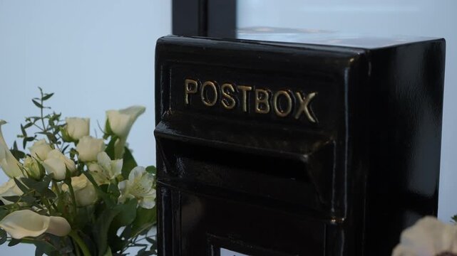 Black Postbox Next To White Bouquet. CloseUp Of Glossy Black Metal Postbox Labeled POSTBOX Sitting On Windowsill Beside Elegant White Calla