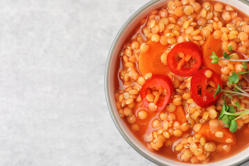 Delicious lentil soup with vegetables in bowl on grey table, top view. Space for text