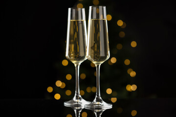 Merry Christmas and Happy New Year. Flute glasses with sparkling wine on black background against blurred lights