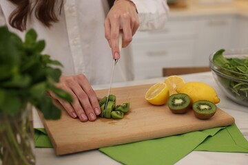 Woman cutting kiwi for blending at white marble table indoors, closeup