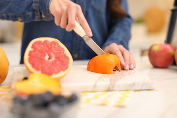 Woman cutting fruits for blending at white marble table indoors, closeup