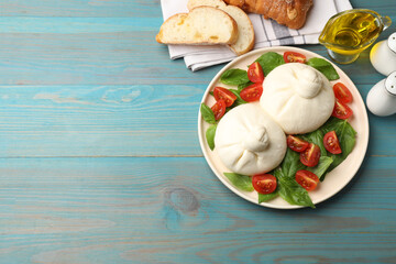 Delicious burrata cheese with tomatoes and basil served on light blue wooden table, flat lay. Space for text