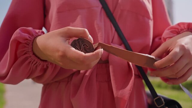 Hands Open Chocolate Coin With Knife, Careful Peel Of Foil Wrapping From HeartStamped Candy CloseUp Of Fingers And Pink Jacket Sleeve, Outdoor Park Background, Casual Snack Moment, Summer Light