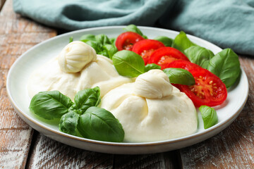 Delicious burrata cheese with basil and tomatoes on wooden table, closeup