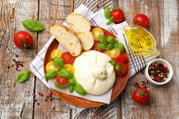 Delicious burrata cheese with basil, bread and tomatoes on wooden table, flat lay