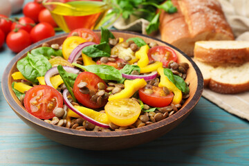 Tasty lentil salad, ingredients and bread on light blue wooden table, closeup