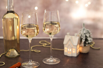 Glasses of white wine and Christmas decor on grey table against background with blurred lights