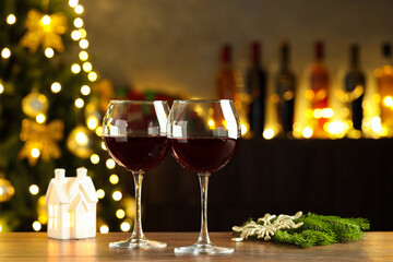 Glasses of red wine and Christmas decor on wooden table indoors