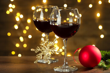 Glasses of red wine and Christmas decor on wooden table against background with blurred lights