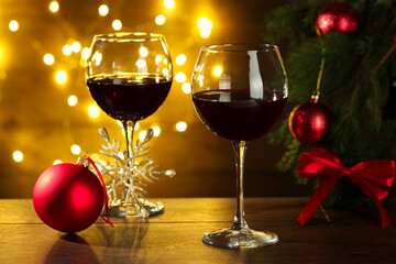 Glasses of red wine and Christmas decor on wooden table against background with blurred lights
