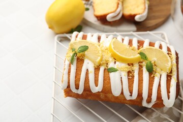 Delicious lemon cake with glaze, fresh fruit slices and mint on white tiled table, closeup. Space for text