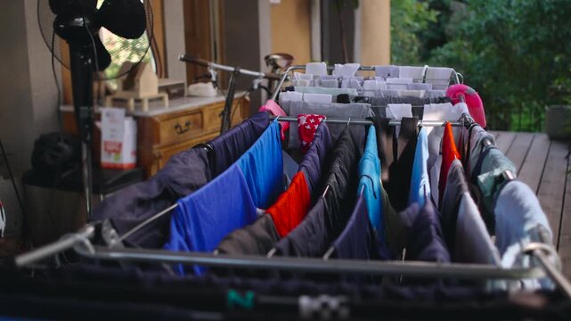 Laundry drying rack lined with colorful garments on balcony with interior softly blurred behind, everyday domestic moment expressing quiet rhythm of home and intimate lived presence