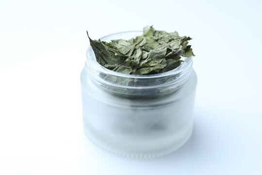 Dried hemp leaves in glass jar on white background, closeup
