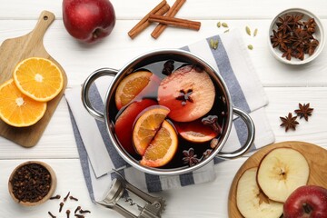 Tasty mulled wine in pot and ingredients on white wooden table, flat lay