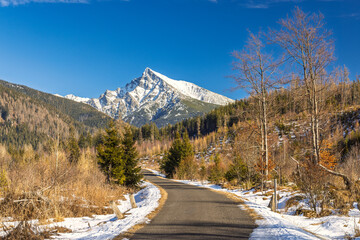 Krivan mountain in High Tatras National Park, Slovakia, Europe. Scenic road winds through a forested landscape towards a snow-capped mountain peak on a clear, sunny day adventure.