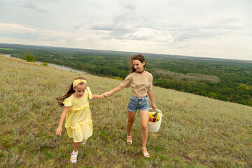 Family on a meadow, mother and daughter holding hands while carries picnic basket
