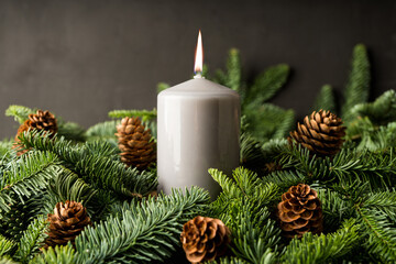 Festive glow: A candle among fir branches and cones. Cozy winter mood. Selective focus.