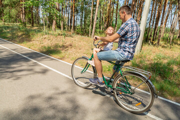 Young father with his little daughter on bicycle in summer sunny forest