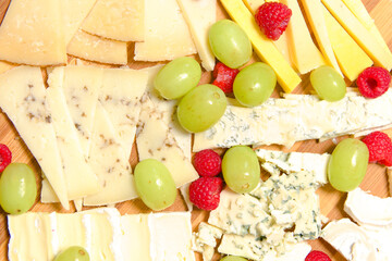 Board of different types of cheeses with raspberries and grapes.