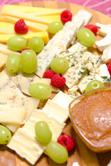 Board of different types of cheeses with raspberries and grapes.