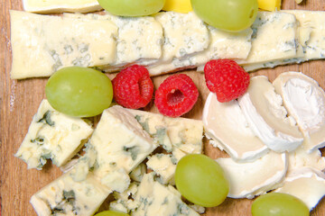 Board of different types of cheeses with raspberries and grapes.