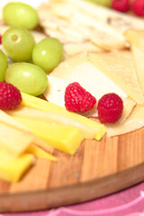 Board of different types of cheeses with raspberries and grapes.
