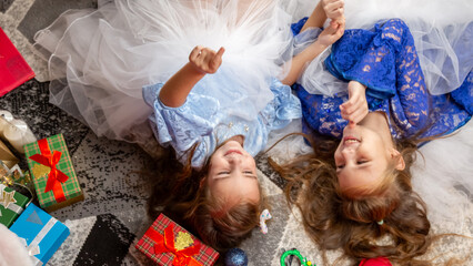 Top view cute children play lying on the floor in a festively decorated room, against the background of a Christmas tree