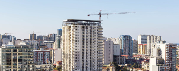Modern residential high rise under construction with tower crane in growing coastal city, urban real estate development, apartment building exterior, investment property, horizontal banner, blue sky © Evgeniia Primavera